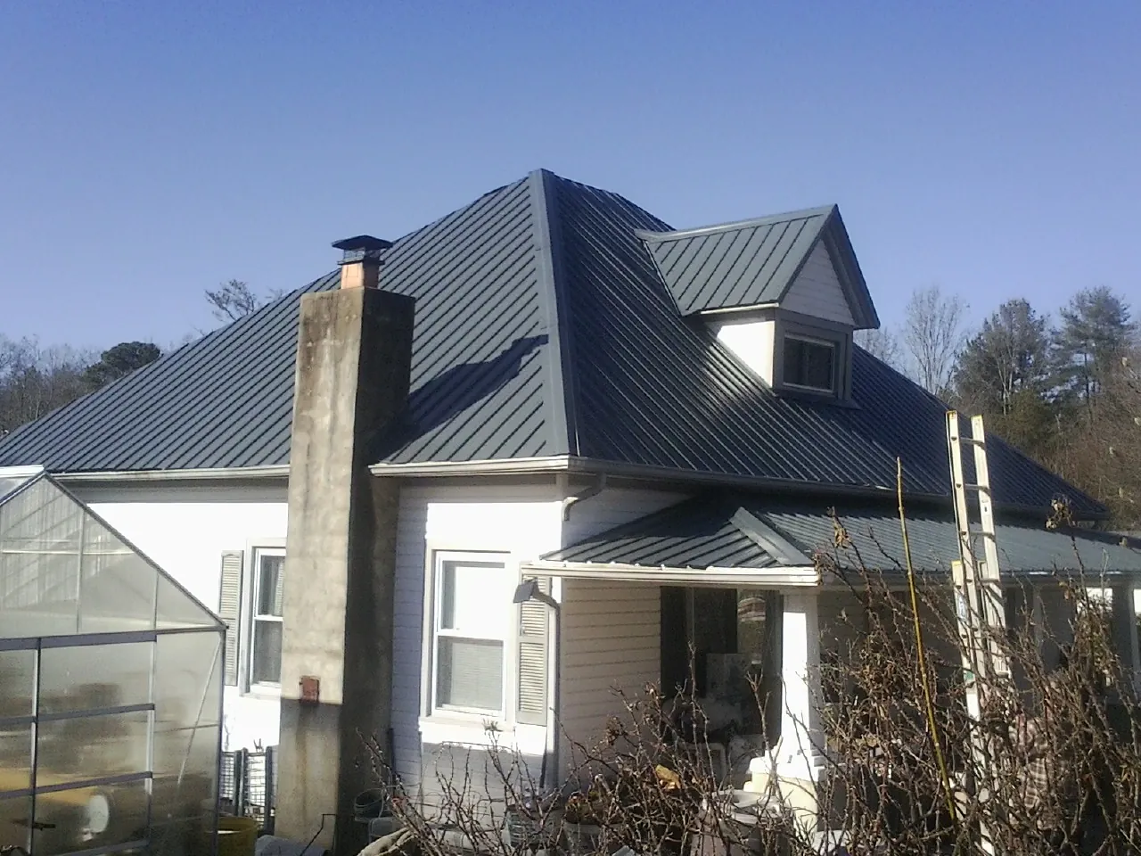 Dark blue standing seam metal roof on a white farmhouse with dormer — Slate & Tile Roof Repair by Roofing Brothers in Hacksneck