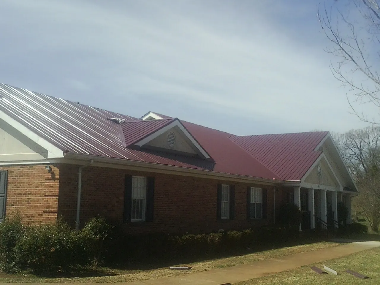 Red metal roof with gabled entries on a long brick building, from a Hail Damage Roof Repair job in Hacksneck