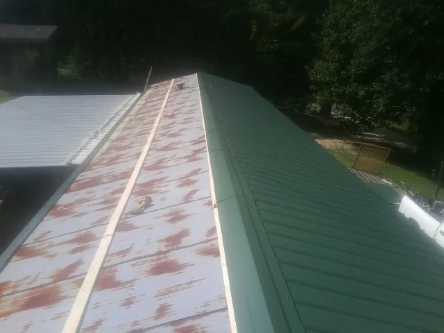 Old rusted panels beside newly installed green metal roofing — Wind Damage Roof Repair by Roofing Brothers in Hacksneck