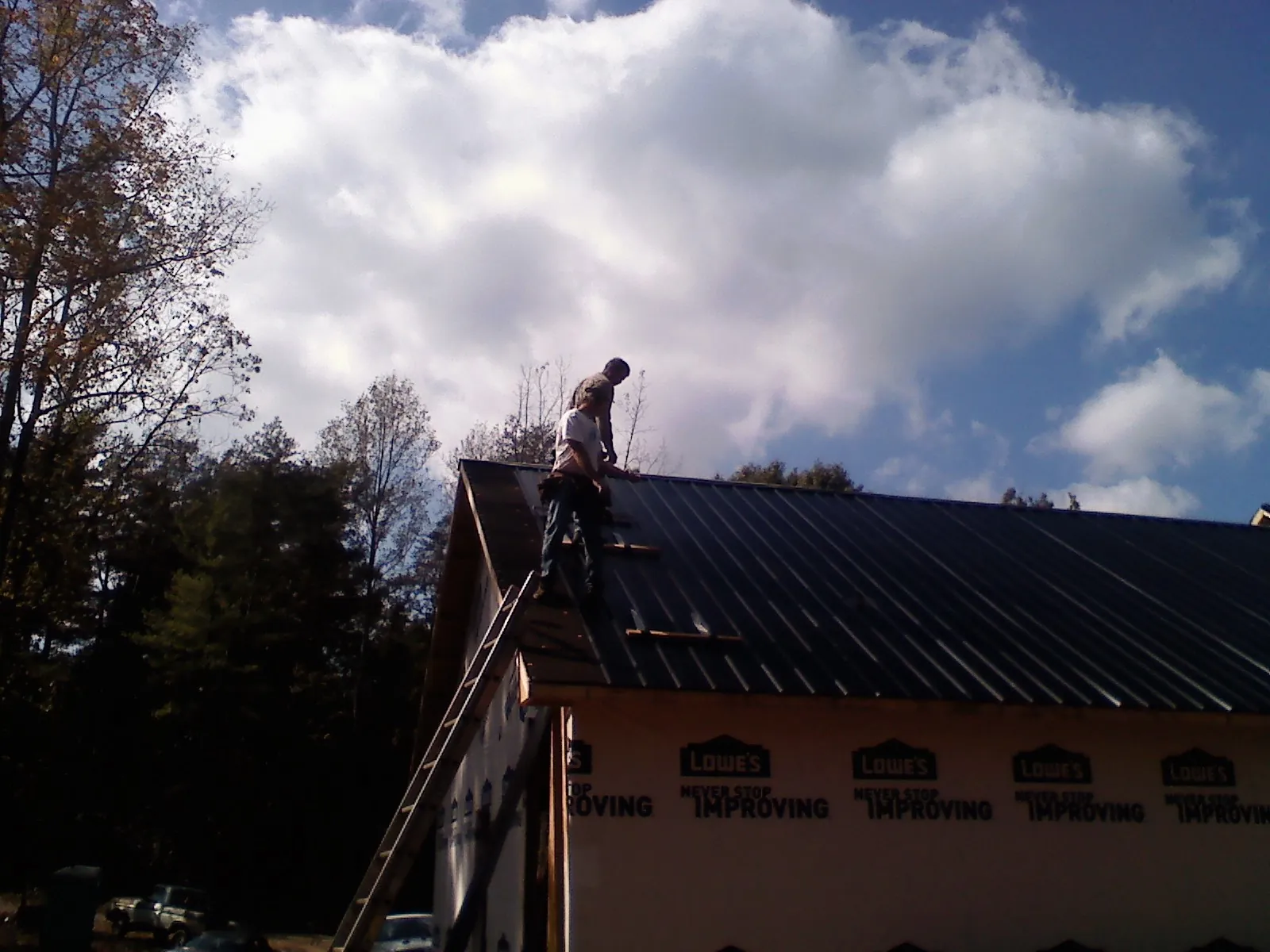 Roofer fastening dark metal panels high against a cloudy sky, from a Roof Inspection job in Hacksneck