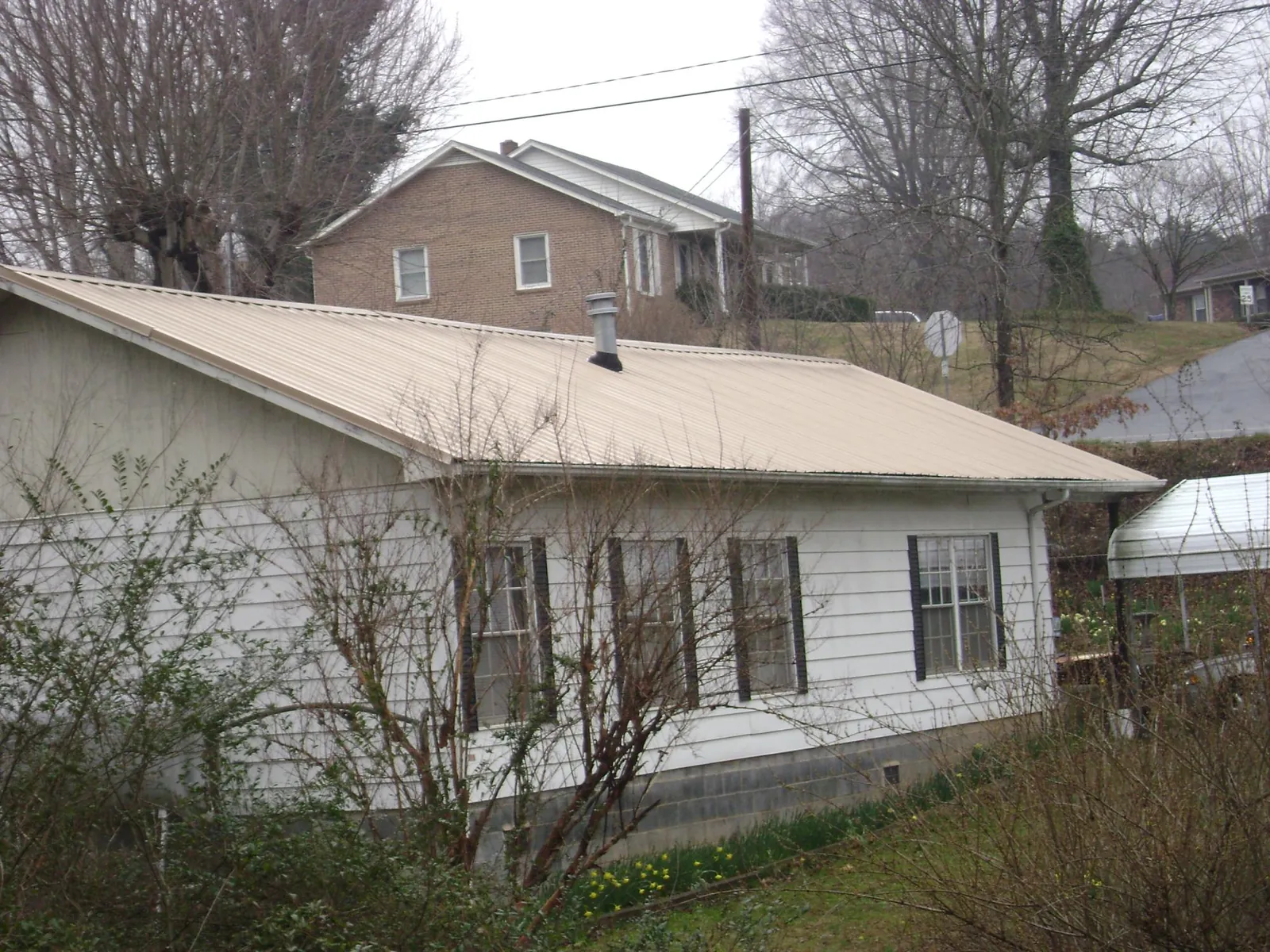 Tan metal roof on a white sided house set into a hillside — Commercial Roofing by Roofing Brothers in Hacksneck